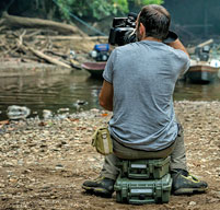 photographer sat on an explorer case near a river taking a picture